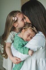 Young beautiful dark-haired mother in light clothes with her little daughters in a cozy house. Little sisters. Girls. Family. Happy motherhood.