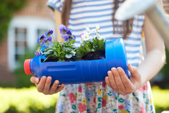 Close Up Of Girl Holding Recycled Plant Holder From Plastic Bottle Packaging Waste In Garden At Home