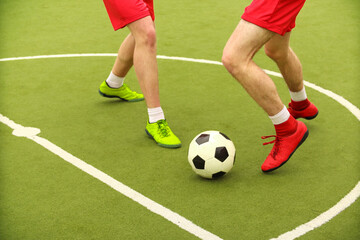 Players play mini football on the field. Legs, sneakers and a ball. Green football field.