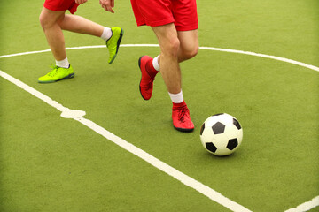 Players play mini football on the field. Legs, sneakers and a ball. Green football field.