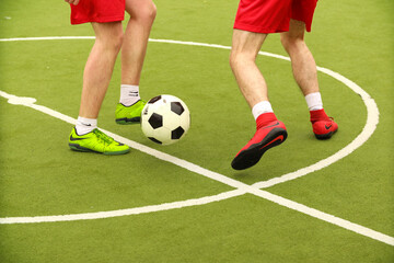 Obraz premium Players play mini football on the field. Legs, sneakers and a ball. Green football field.