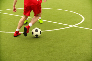 Players play mini football on the field. Legs, sneakers and a ball. Green football field.