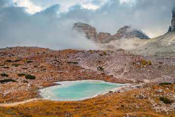 Tre Cime Di Lavaredo National Park in the morning mist. Gloomy autumn view of frozen Rienzquelle lake. Trekking in Dolomite Alps, Italy, Europe. Beauty of nature concept background.