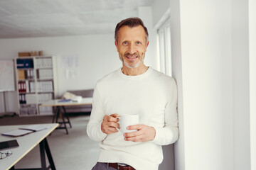 A businessman with white turtleneck sweater stands with a cup in the office