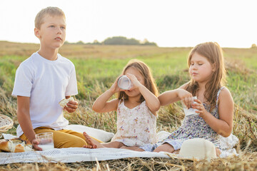 Portrait of meditative children boy and two girls sitting on blanket in field, having picnic,...