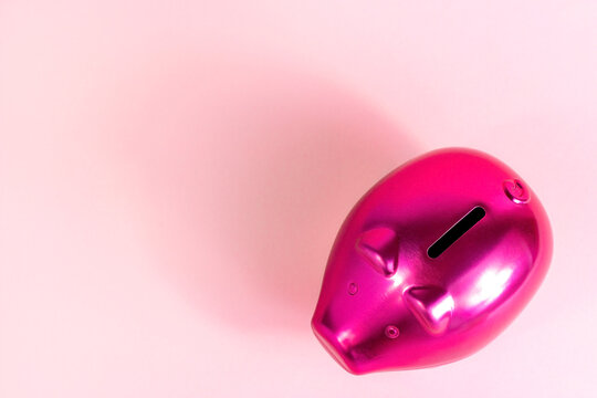 Bright pink piggy bank for coins on light rose background with copy space top view.