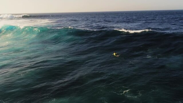 Lonely surfer swimming towards massive ocean waves, aerial view