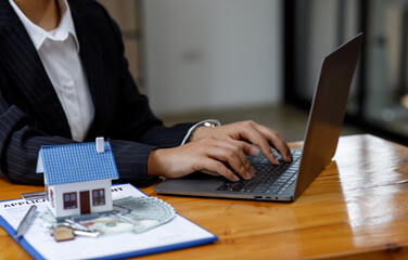 Businesswoman realtor taking notes and holding house model, sitting at desk with paper house model and keys, female real estate agent manager, preparing documents, mortgage and property.