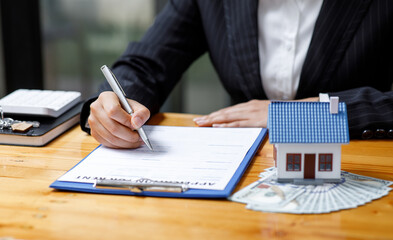 Businesswoman realtor taking notes and holding house model, sitting at desk with paper house model and keys, female real estate agent manager, preparing documents, mortgage and property.