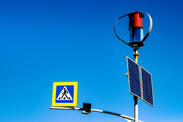 Wind generator and solar panels for a traffic light at a pedestrian crossing, against the backdrop of a beautiful blue sky.