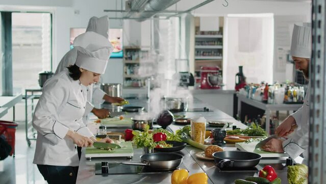 Woman chef using knife to cut garlic clove on cutting board, adding organic aromatic ingredient to make delicious dish. Person in uniform cooking gourmet food recipe in professional kitchen.