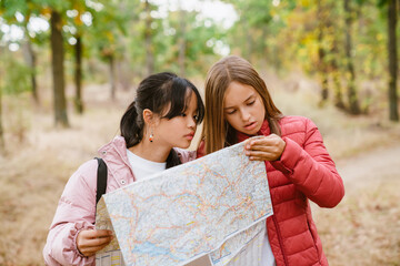 Multiracial teenagers examining map during hiking in forest