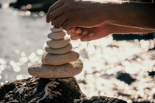Man bilds stones pyramid on the seashore on a sunny day on the blue sea background. Happy holidays. Pebble beach, calm sea, travel destination. Concept of happy vacation on the sea, meditation, spa