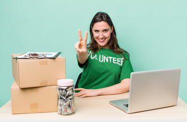 young pretty woman  smiling and looking happy, gesturing victory or peace. volunteer donation...