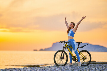 Active young one slim fit happy joyful carefree inspired woman bicycler with closed eyes and outstretched arms wearing sportswear standing alone with bicycle outdoors