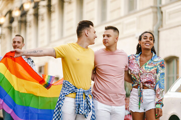 Young gay people holding rainbow flag during pride parade on street