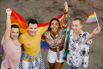 Young gay people smiling and holding rainbow flag during pride parade