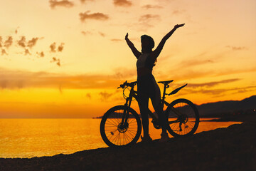 Silhouette of active one free happy joyful carefree inspired woman bicycler with open arms standing alone with bicycle outdoors against sunset sky - Powered by Adobe