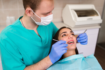 A male dentist examines a patient's teeth using a professional dental microscope. The client lies on the dentist's chair.