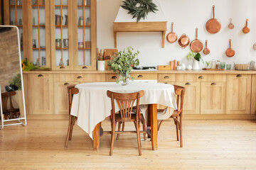 Stylish dining room with furniture in retro style. Cozy Wooden cuisine decorated with summer decor. Kitchen utensils, dishes, plates. Interior design scandinavian kitchen with round table and chairs	