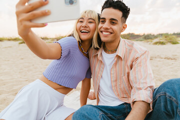 Young multiracial couple taking selfie photo on cellphone on beach