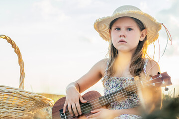 Portrait of girl sitting on blanket in dry hay field, having picnic, learning playing ukulele....