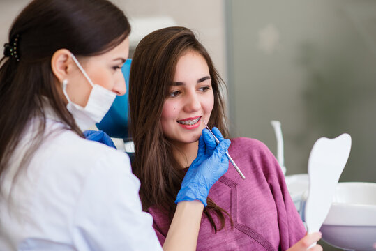Smiling young girl is looking in mirror for estimating dentist work and enjoying result with specialist