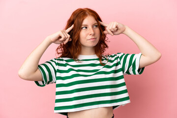 Teenager redhead girl over isolated pink background having doubts and thinking