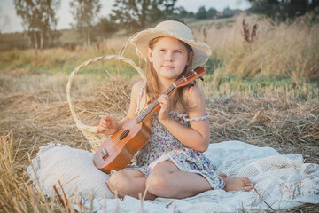 Portrait of smiling girl sitting on blanket in dry hay field, having picnic, learning playing...
