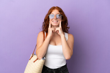 Teenager redhead girl holding a beach bag isolated on purple background smiling with a happy and pleasant expression