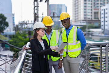 caucasian businesswoman in black suit wear helmet working on tablet with black engineers outside building in city