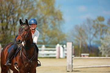 Young woman sits on her horse, woman smiles at the camera and puts her hands around the horse's neck..