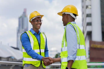 black engineers shake hand together at outside building in city after success job. black engineer in glow shirt and helmet