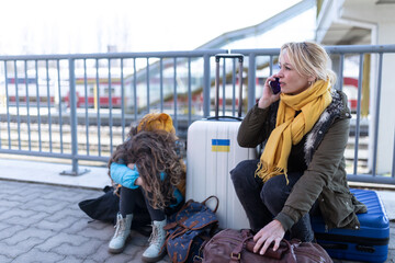 Sad Ukrainian immigrants family with luggage waiting at train station, Ukrainian war concept.