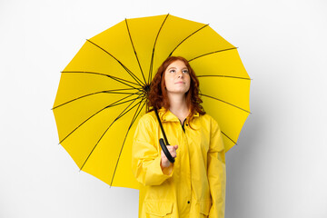 Teenager redhead girl rainproof coat and umbrella isolated on white background and looking up