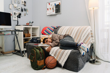 Black boy sleeping while doing homework on sofa at home