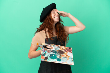 Teenager redhead artist holding a palette isolated on green background smiling a lot