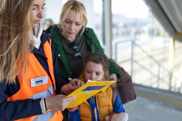 Volunteer filling form for Ukrainian refugees at train station. - obrazy, fototapety, plakaty