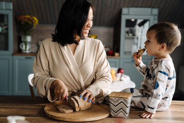 Happy mother making fun with her son while cutting bread