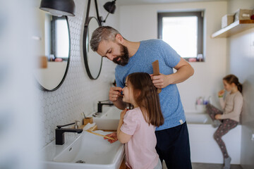 Father brushing his little daughter's hair in bathroom, morning routine concept.