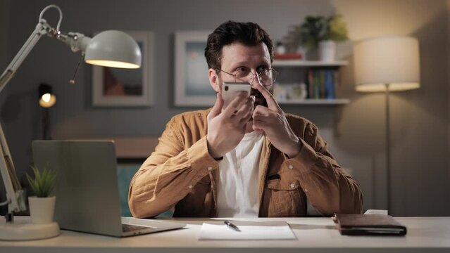 Man with phone records voice message. Bearded freelancer at home office using voice translator. Remote worker dictating text to virtual assistant on phone
