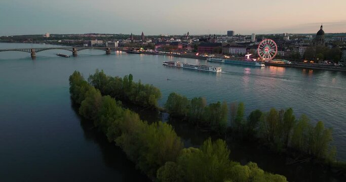 Sunset drone flight of Mainz over the Rhine river crossing a boat with a wine fest at the riverbank and summer evening sky in the back