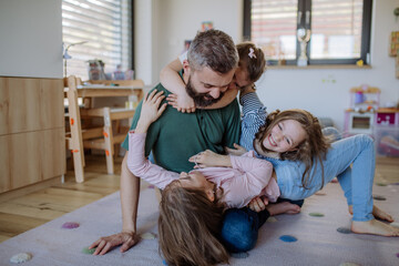 Cheerful father with three little daughters playing together at home.