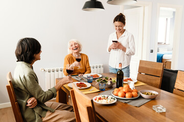 Mature three women talking and laughing while having dinner in kitchen
