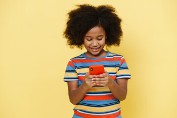Black preteen girl with curly hair smiling and using cellphone