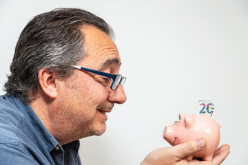 Mature man holding and smiling to a piggy bank containing bills