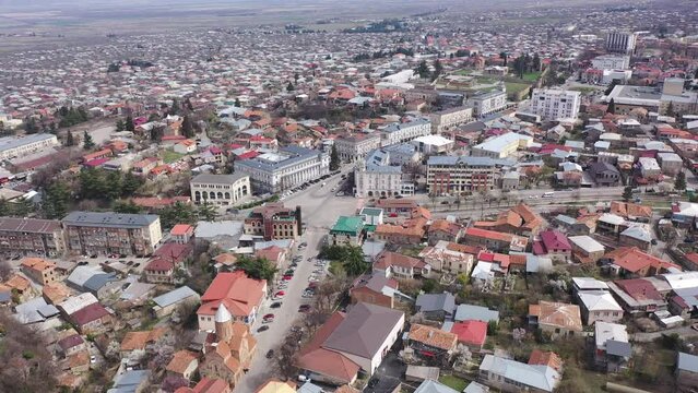 Scenic view from drone of central area of Telavi city overlooking large avenue with modern buildings surrounded by old small houses on spring day, Georgia