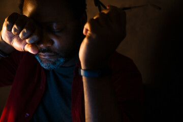 Obraz premium Black tired man holding eyeglasses while rubbing his eye