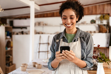 Young black ceramist woman using cellphone while working in her studio