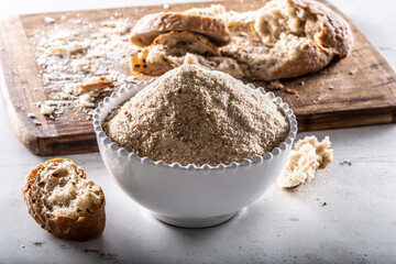 A white bowl full of breadcrumbs and old dry bread around